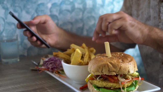 Man Eating Burger with French Fries and Chatting on Phone