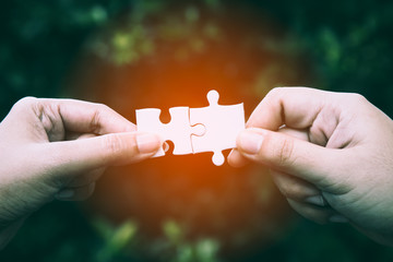 Close up of two hands trying to connect couple puzzle piece with forest background; one part of...