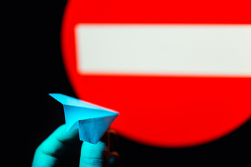 Woman hold small paper aircraft in hand against prohibiting sign in background. Airplane is logo of...