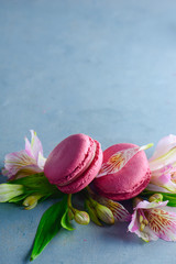 Pink macaroons decorated with pink and white alstroemeria flowers. Romantic French dessert on stone background with copy space.