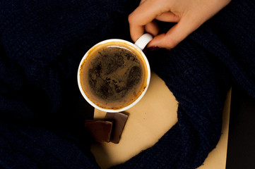 female hand in sweater holds a cup of coffee and chocolate pieces of blue wrap, autumn mood
