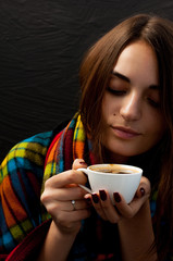 young pretty girl with wrap on her shoulders holding a cup of coffee thoughtfully looking into the cup, cute portrait