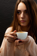 young beautiful girl in a warm sweater holds a cup of coffee thoughtfully looking sideways, cute portrait