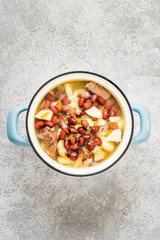 Bean and bacon soup in a pot on concrete background. Top view, space for text.