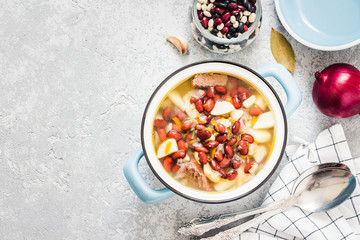 Bean parmesan spinach soup in a pot on concrete background. Top view, space for text.