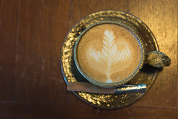 hot latte coffee gold cup with art and graphic show on cup on the gold table woden