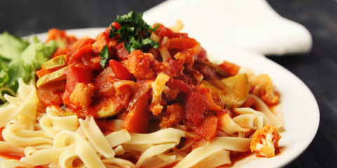 Ribbon pasta with Arrabiata sauce. Close up. Mediterranean dish. Tagliolini pasta with vegetables. Cauliflower, courgette and tomato stew. Italian cuisine. Vegan and vegetarian. Wide photo.