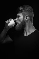 Black and white side view portrait of bearded brutal young man drinking morning espresso coffee to go Hipster holding to go cup of coffee and drinking expresso.