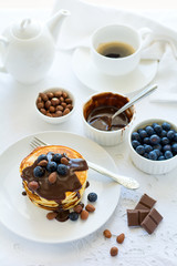 Traditional breakfast concept. Stack of pancakes with chocolate sauce, blueberries and nuts on white table cloth. Selective focus