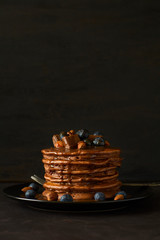 Stack of chocolate pancakes with icing, blueberry, almond, hazelnut and pieces of chocolate. Selective focus.