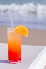 Glasses with colored cocktails on the beach with blue water in the background. Toned