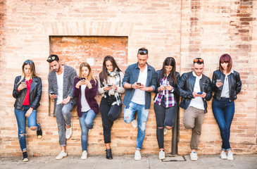 Friends group using smartphone against wall at university college backyard break - Young people...