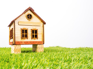 Fototapeta na wymiar Model traditional wooden house on stilts. Wooden house toy on green grass. Isolated wooden toy house with pier angle view. Concept of the Earth Day. Copy space
