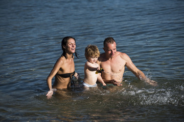 Father and mother swim with son in sea. Family spend time together and having fun. Cute child boy play with toy in ocean, sea, with parents. Family vacation concept. Young family swimming on sunny day