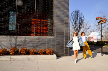 Obraz premium Fashionable urban girls wearing trendy outfit with balloons walking on New York City street.
