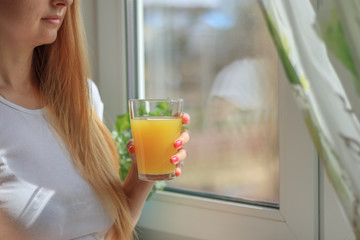 Young blonde woman drinking orange juice and looking at the window