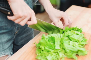 Close-up Female hands chopping a green plant salad cooking salad from vegetables on a wooden cutting board at home. The concept of vegetarianism and healthy lifestyles