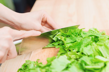 Close-up Female hands chopping a green plant salad cooking salad from vegetables on a wooden cutting board at home. The concept of vegetarianism and healthy lifestyles