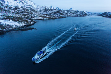 Fisher boat going for fishing before sunrise with mountains full of snow in background. Lofoten Island, Norway.