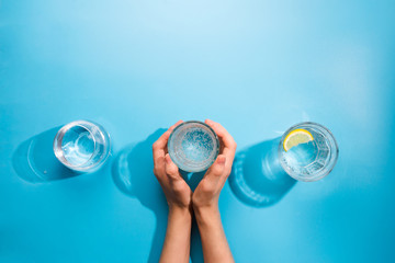 Flatlay of woman's hands holding a cup of clean sparkling water. Healthy concept, blue background
