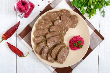 Home made dietary sausage from the liver on a white wooden table. Sausage cut into pieces on a plate with horseradish sauce. Top view.