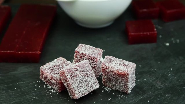 confectionery hand lays out small piece of handmade crimson marmalade coated with sugar into group on black stone background