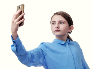 Young girl taking self portrait with her smartphone, blue shirt, white background, Serious face expression.