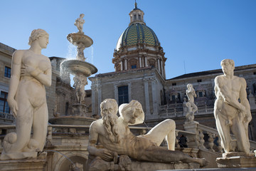 Group of white marble statues part of the Pretoria Fountain of Palermo. Statues of naked woman and man, and Poseidon laying down. With church dome at background. Ita: Fontana Pretoria, Palermo.