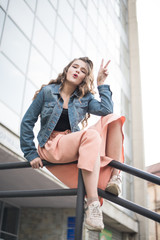 Portrait of a beautiful teenage girl. Happy hipster woman having fun on interesting city background. Pretty teenage girl. Fashionable portrait of beautiful girl. Model. Fashion. showing peace sign.