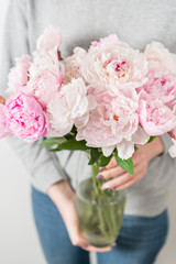 Cute and lovely peony flowers in women's hands.. many layered petals. Bunch pale pink peonies flowers light gray background. Wallpaper, Vertical photo