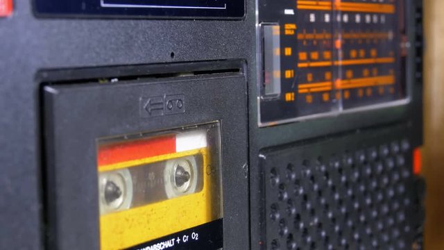 The Vintage Yellow Audio Cassette in the Old Tape Recorder Rotates. Macro static camera view of a vintage audio cassette tape with a blank label in use sound recording in a cassette player. Radio