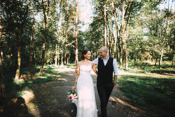 The newlyweds. Wedding day. Loving couple walking in the park at sunset. Bride in a beautiful wedding dress, groom in a stylish tuxedo