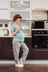 Fototapeta na wymiar Pregnant woman using a smartphone standing in the kitchen