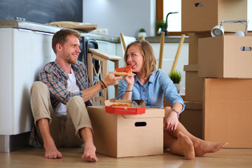 Fototapeta na wymiar Young couple have a pizza lunch break on the floor after moving into a new home with boxes around them. Young couple