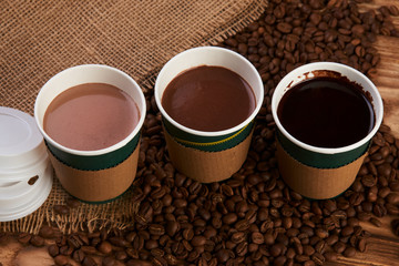 Three take away green paper cups with coffee beans and hot chocolate drink on wooden background, top view, close-up