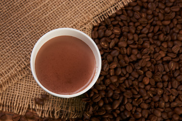 Take away coffee paper cup with hot chocolate drink and roasted coffee beans on wooden table background with copy space, top view, close-up
