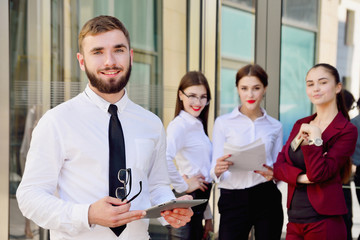 Businessman man with a tablet in his hands shows a thumb to the top against the background of the girls. Office staff in the background of a multi-storey glass building. Lifestyle. Manager
