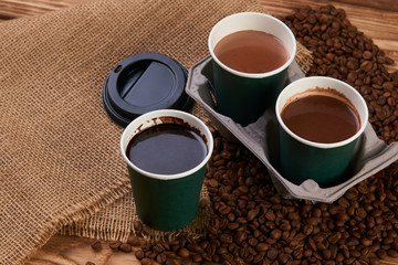 Close-up of three take away green paper cups in coffee holder container with coffee beans and hot chocolate drink on rustic wooden table background, top view, 