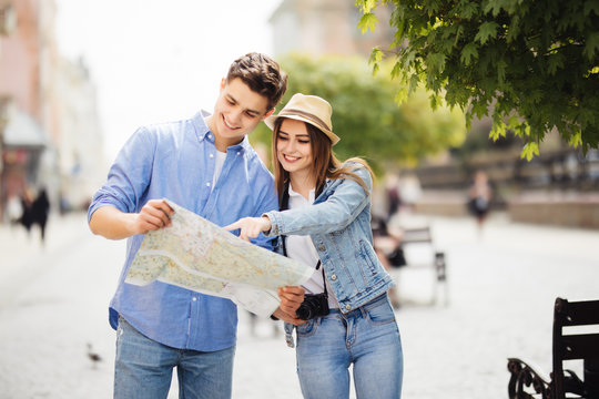 Young Couple of tourists is exploring new city together. Smiling and look at the map on the city street