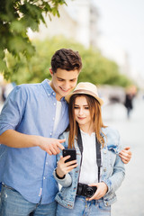 Happy young couple look at phone screen to app of tourists sightseeing in the street