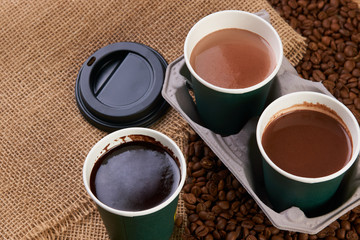Three cardboard coffee cups. Take away green paper cups with coffee beans and hot chocolate drink on wooden background