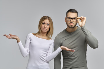 young beautiful couple carefully considered and surprised what they see spreading their hands to sides 