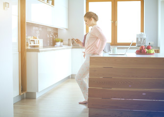 Woman using mobile phone standing in modern kitchen.