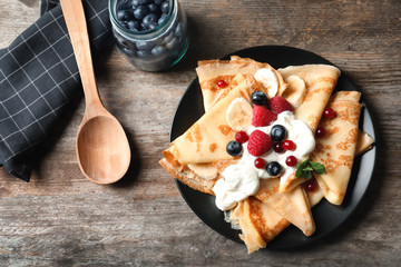 Thin pancakes with berries and cream on plate, top view - obrazy, fototapety, plakaty
