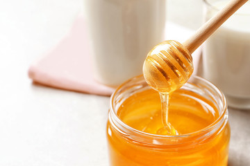 Fototapeta na wymiar Honey pouring from dipper into jar, closeup