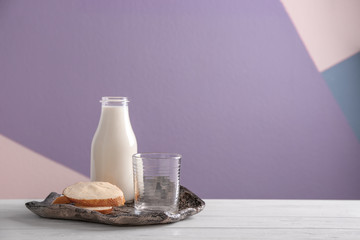 Bottle of milk and sliced bread with butter on table against color background