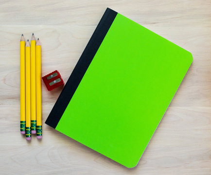Back to school-4 yellow pencils, a red pencil sharpener and a green notebook with blank cover for customized message, all on a wooden desk