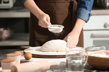 Obraz na płótnie Canvas Woman sprinkling flour over dough on table in kitchen