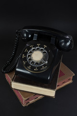 retro black telephone with rotary dial and cord on worn books