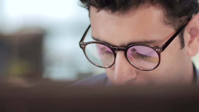  Reflection of computer screen can be seen in the eyeglasses of an handsome male entrepreneur in modern corporate office 